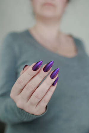 Female hand with long nails and purple plum manicure holds a bottle of nail polishの写真素材