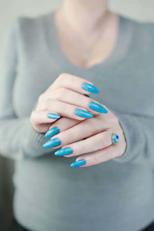Woman's beautiful hand with long nails and light blue manicure with bottles of nail polishの写真素材