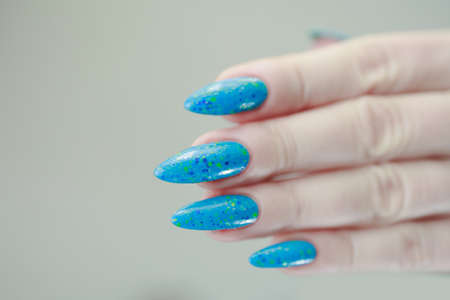 Woman's beautiful hand with long nails and light blue manicure with bottles of nail polishの写真素材