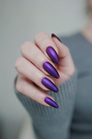 Female hand with long nails and purple plum manicure holds a bottle of nail polishの写真素材
