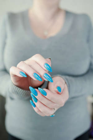 Woman's beautiful hand with long nails and light blue manicure with bottles of nail polish