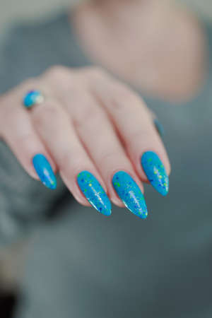 Woman's beautiful hand with long nails and light blue manicure with bottles of nail polishの写真素材