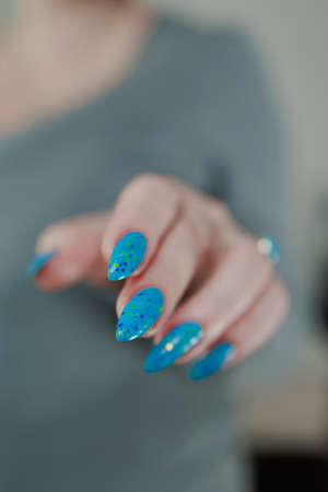 Woman's beautiful hand with long nails and light blue manicure with bottles of nail polishの写真素材