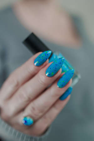 Woman's beautiful hand with long nails and light blue manicure with bottles of nail polishの写真素材