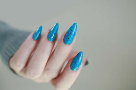 Woman's beautiful hand with long nails and light blue manicure with bottles of nail polishの写真素材