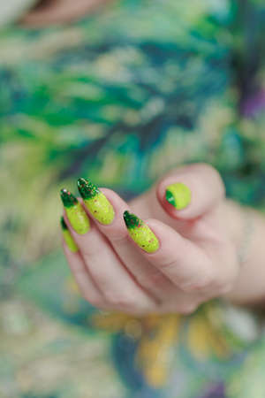 Woman's hand with long nails and bright yellow green thermo manicure with bottles of nail polishの写真素材