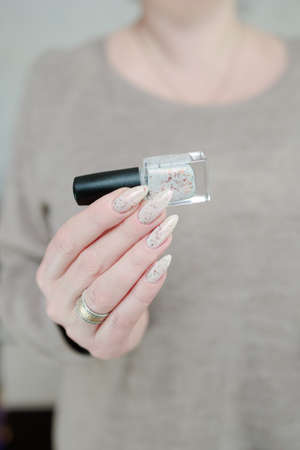beautiful female hands with long nails light white manicure and a bottle of nail polish