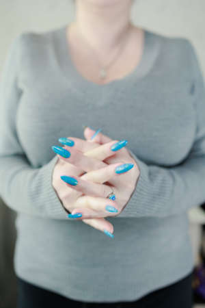 Woman's beautiful hand with long nails and light blue manicure with bottles of nail polish