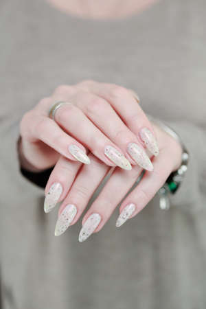 beautiful female hands with long nails light white manicure and a bottle of nail polishの写真素材