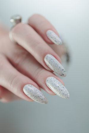 beautiful female hands with long nails light white manicure and a bottle of nail polishの写真素材