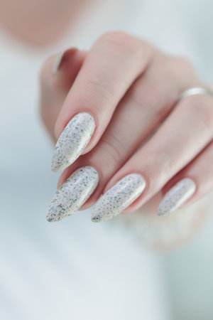 beautiful female hands with long nails light white manicure and a bottle of nail polishの写真素材