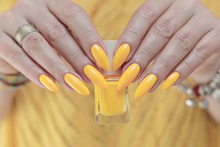 Female hand with long nails and a bottle of bright yellow orange neon nail polishの写真素材