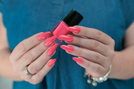 Female hand with long nails and a bottle bright neon pink red color nail polish