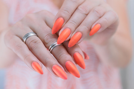 Female hands with long nails and neon orange coral nail polish