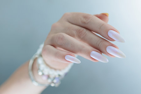 beautiful female hands with long nails light white and blue manicure and a bottle of nail polishの写真素材