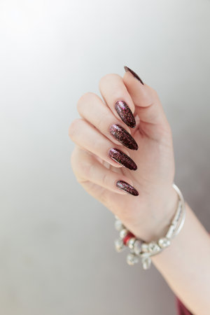Woman hands with long nails and a bottle of dark red burgundy nail polishの写真素材