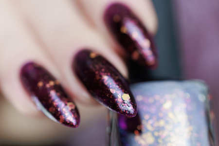 Woman hand with long nails and a bottle of dark purple burgundy nail polishの写真素材