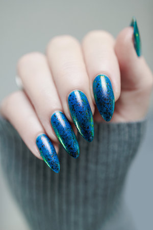 Woman's beautiful hand with long nails and blue green manicure with bottles of nail polishの写真素材
