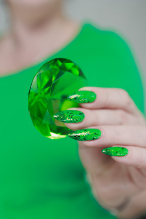 Female hands with long nails and green and black thermo manicure with bottles of nail polish