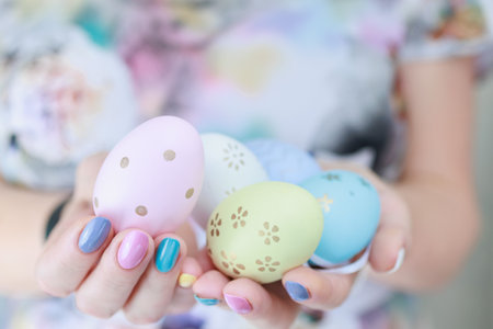 Women's hands with multi-colored manicure hold Easter eggs. Light yellow, blue and pink color.