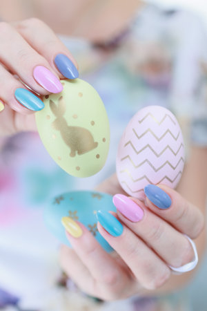 Women's hands with multi-colored manicure hold Easter eggs. Light yellow, blue and pink color.の写真素材