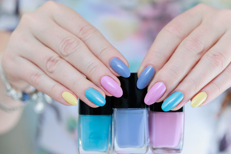 Multicolored manicure, female hands hold bottles of nail polishes, yellow, blue and pink colorの写真素材