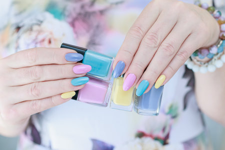 Multicolored manicure, female hands hold bottles of nail polishes, yellow, blue and pink colorの写真素材