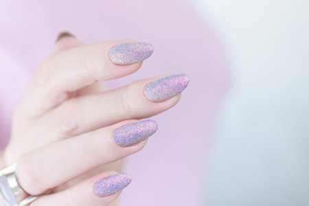 Woman's hands with long nails and a bottle of light pink and blue color nail polishの写真素材