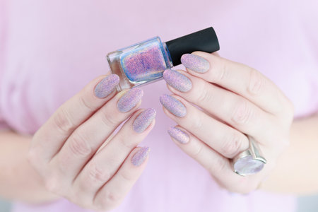 Woman's hands with long nails and a bottle of light pink and blue color nail polish