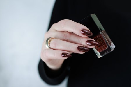 Woman hand with long nails and a bottle of dark red burgundy nail polishの写真素材