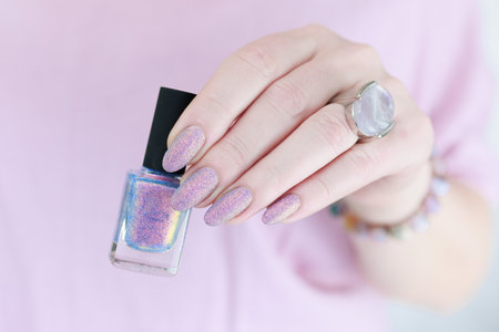Woman's hands with long nails and a bottle of light pink and blue color nail polish