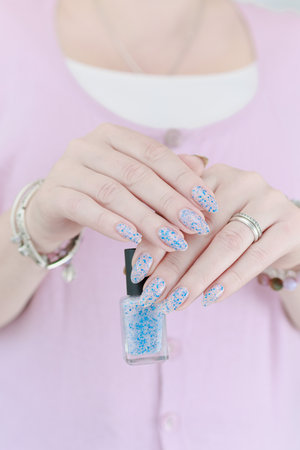 Woman's hands with long nails and a bottle of light pink and blue color nail polish
