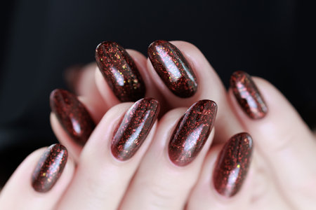 Woman hand with long nails and a bottle of dark red burgundy nail polish