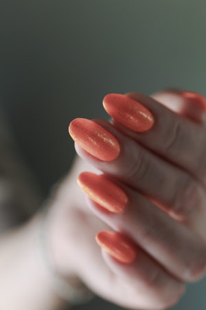 Woman's hands with long nails and a bottle of orange nail polishの写真素材