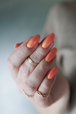 Woman's hands with long nails and a bottle of orange nail polish