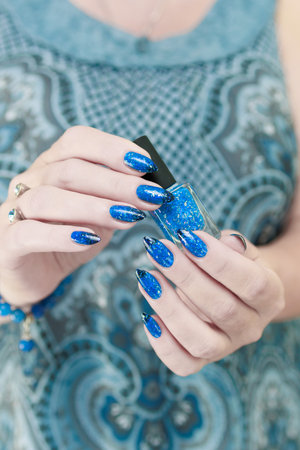 Woman's beautiful hand with long nails and blue manicure with bottles of nail polishの写真素材