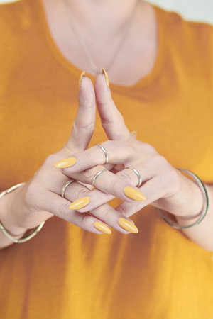 Female hand with long nails and a pale yellow manicure hold bottles of nail polishの写真素材