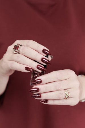 Woman hand with long nails and a bottle of dark red burgundy nail polishの写真素材