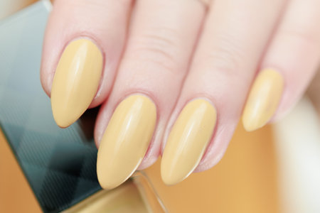 Female hand with long nails and a pale yellow manicure hold bottles of nail polish