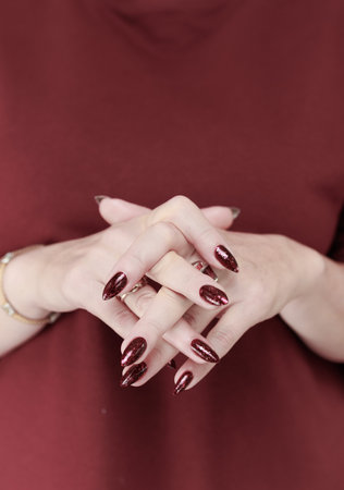 Woman hand with long nails and a bottle of dark red burgundy nail polishの写真素材