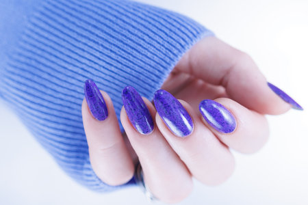Female hand with long nails and a bottle of light blue lilac color nail polishの写真素材