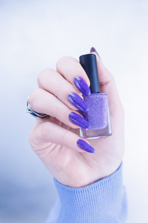 Female hand with long nails and a bottle of light blue lilac color nail polishの写真素材
