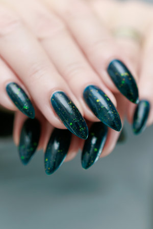 Woman's beautiful hand with long nails and dark teal, blue and green nail polish