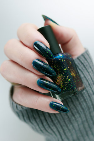 Woman's beautiful hand with long nails and dark teal, blue and green nail polish