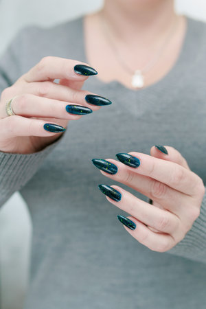 Woman's beautiful hand with long nails and dark teal, blue and green nail polish
