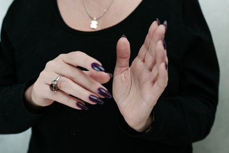 Female hand with long nails and purple plum manicure holds a bottle of nail polishの写真素材
