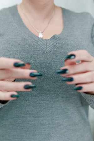 Woman's beautiful hand with long nails and dark teal, blue and green nail polish