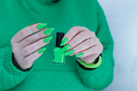 Female hand with long nails and neon green manicure with bottles of nail polishの写真素材