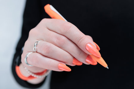 female hand holding an orange pen on a black backgroundの写真素材