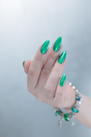 Female hand with long nails and bright green manicure with bottles of nail polishの写真素材